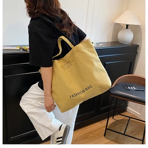 Close-up of yellow canvas tote bag with fashion text detail and sturdy fabric texture