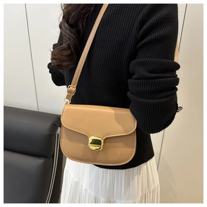 Détail d'un sac besace kaki avec boucle dorée porté par un mannequin dans un style chic
