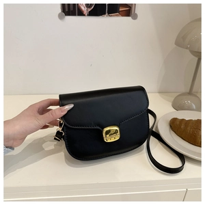 Détail d'un sac besace noir avec boucle dorée carrée sur un bureau minimaliste