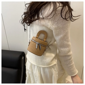 Rear view of model wearing a mini woven bucket bag with leather trim and chain strap
