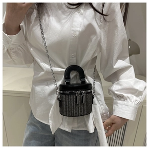 Close-up of a mini cylindrical woven bucket bag with silver chain and leather handle