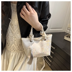 Detailed close-up of embroidered floral pattern on beige bucket bag with tassel detail
