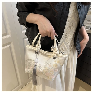 Detail of embroidered silk bucket bag with woven handle and elegant grey silk tassel