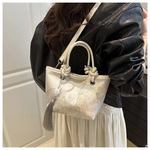 Detail of embroidered floral bucket bag with silk finish, fringe tassel and woven handle