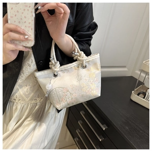 Detail of floral embroidery on a cream bucket bag with silk tassel and rope handle