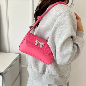 Pink shoulder bag with woven texture and silver bow detail worn by a model in a bright room