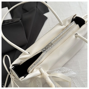 Dettaglio della borsa in pelle PU bianco crema con zip argentata e fiocco in pizzo bianco