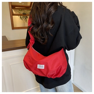 Detail of red nylon pleated shoulder bag with white fabric label on black hoodie background