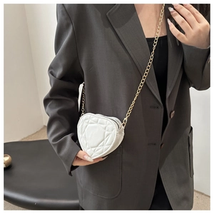 Detailweergave van witte hartvormige crossbodytas met gewatteerd patroon en gouden ketting