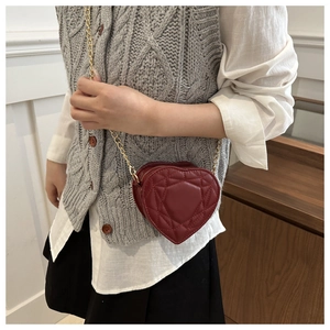 Detail shot of a red heart-shaped quilted leather crossbody bag with golden chain strap