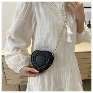 Detail of a quilted black heart-shaped crossbody bag with a sleek gold chain strap