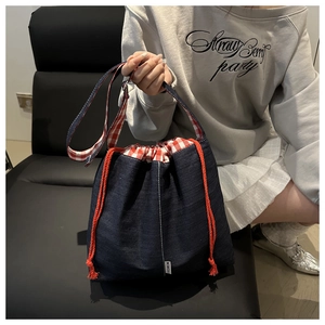 Détail du sac seau en jean bleu montrant la doublure à carreaux rouges et l'étiquette