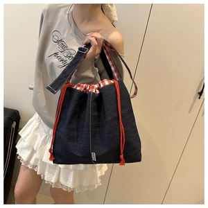 Détail de fermeture à cordon avec doublure vichy sur sac fourre-tout en denim