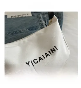 Detail of minimalist cream nylon shoulder bag with YICAIAINI print on denim background
