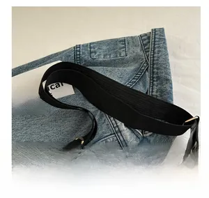 Detail of adjustable black woven strap and metal buckle on washed blue denim tote bag