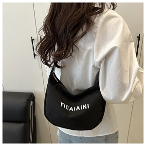 Detail view of large black canvas hobo bag with white letter print worn by a model