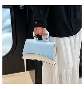 Detail of blue and white two-tone handbag with round silver metal handle and long strap