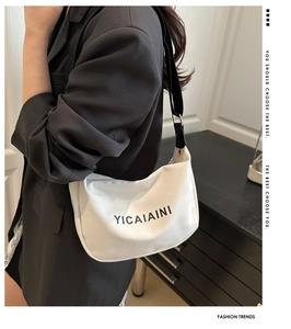 Close-up of white canvas shoulder bag with adjustable black strap worn by a model