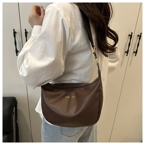 Detail of dark brown crescent bag with gold lettering and wide fabric shoulder strap