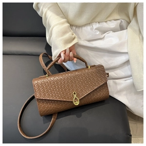 Detail of brown woven baguette bag with a signature gold music note clasp and strap