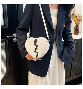 Sac bandoulière blanc en forme de cœur avec éclair noir porté sur blazer bleu