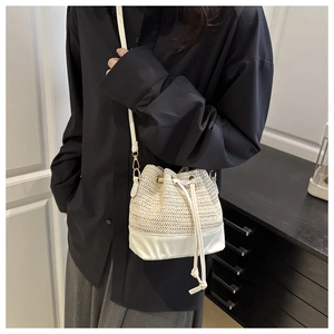 Detail of straw bucket bag with white leather base and drawstring closure on shoulder strap