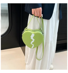 Détail du sac à bandoulière vert clair en forme de cœur avec motif blanc et zip argenté