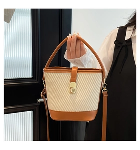 Detail of woven bucket bag featuring brown leather trim and golden clasp closure