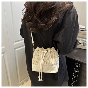 Detail of cream woven bucket bag with leather base and drawstring closure on model
