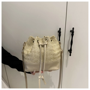 Close-up of woven straw bucket bag with drawstring closure and slim leather strap