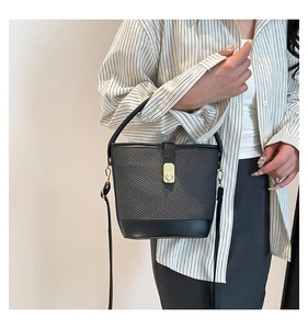 Detail of black woven texture bucket bag with gold metal twist lock and thin strap