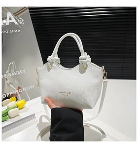 Detail of white lychee pattern crossbody bag with knot handles and golden logo text