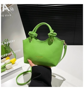 Detail of bright green pebble leather bucket bag with knot handle and golden text logo