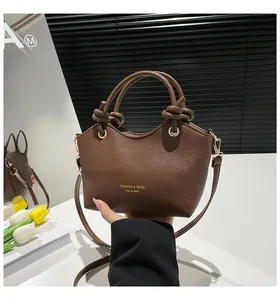Close-up of brown litchi grain leather bucket bag with elegant knotted handles and gold text
