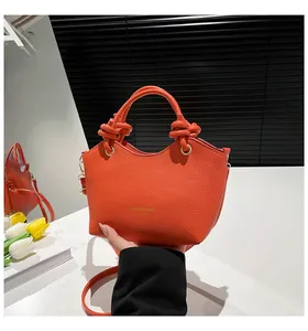Detailed macro view of the bright orange bucket bag featuring textured faux leather and knotted handle