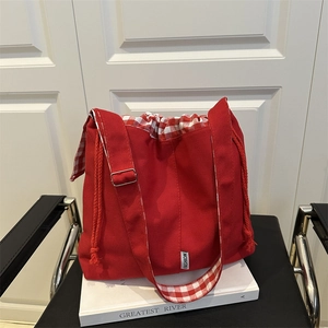 Red canvas drawstring tote bag with plaid lining and adjustable wide shoulder strap