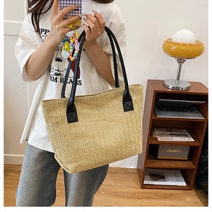 Dettaglio della borsa tote in paglia intrecciata con manici in pelle nera e cuciture rinforzate