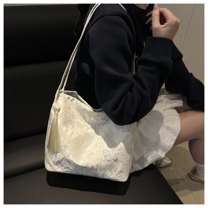Close-up of cream lace shoulder bag featuring butterfly embroidery and tassel detail