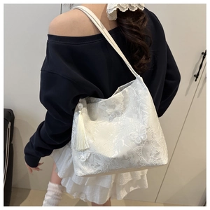 Détail d'un sac cabas en dentelle blanche avec broderie papillon et long gland