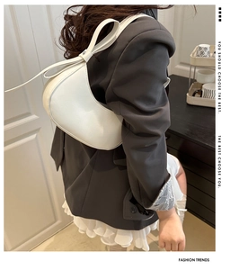 Close-up of a white minimalist underarm bag with a large bow detail on the shoulder strap
