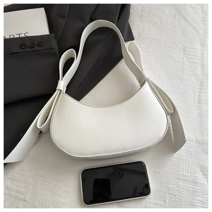 Close-up of a white crescent shoulder bag with bow detail beside a phone for scale