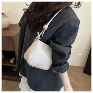 Dettaglio di una borsa a secchiello beige in pelle con nodo decorativo sulla tracolla