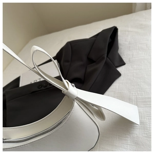 Detail of white half-moon shoulder bag featuring a large bow and smooth PU leather