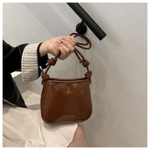 Dettaglio di borsa in pelle lucida marrone con manico a nodo e design vintage chic