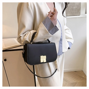 Detailopname van een zwarte crossbody tas met gouden slot op een stijlvol wit pak