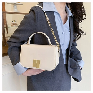 Détail d'un sac bandoulière beige avec boucle dorée et bandoulière chaîne sur un modèle