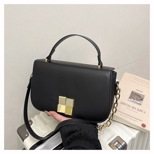 Détail du sac à bandoulière en cuir noir avec chaîne dorée et boucle carrée sur valise