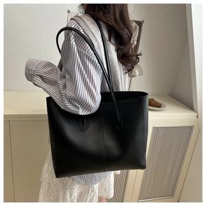 Minimalist large black PU leather tote bag with center seam detail worn over the shoulder