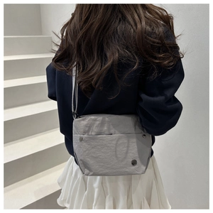 Close-up of minimalist grey nylon crossbody bag with circular metal logo on a model