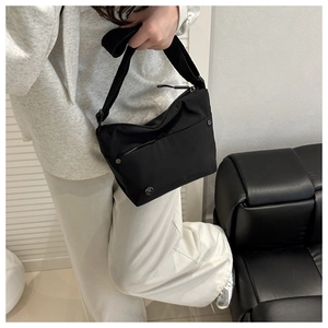 Detail of minimalist black nylon crossbody bag featuring wide strap and metallic logo